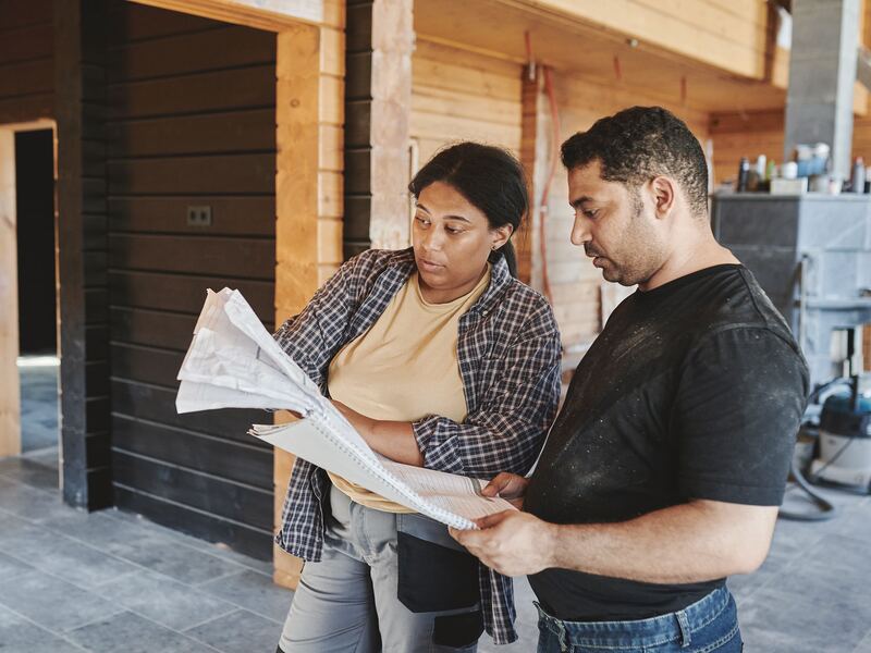 Jefa de obra revisa planos con un compañero dentro de una casa en construcción