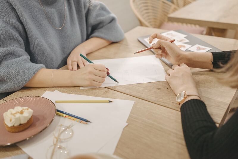 Dos personas dibujan en papel sobre una mesa de trabajo